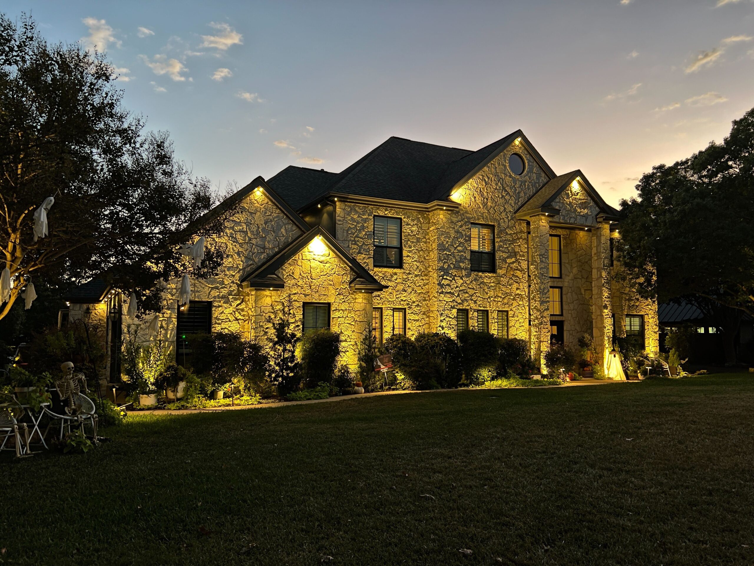 A two-story stone house illuminated with Astoria Permanent Outdoor Lights. The lights are set to a warm yellow color, lining the roof and highlighting the architectural details of the house.