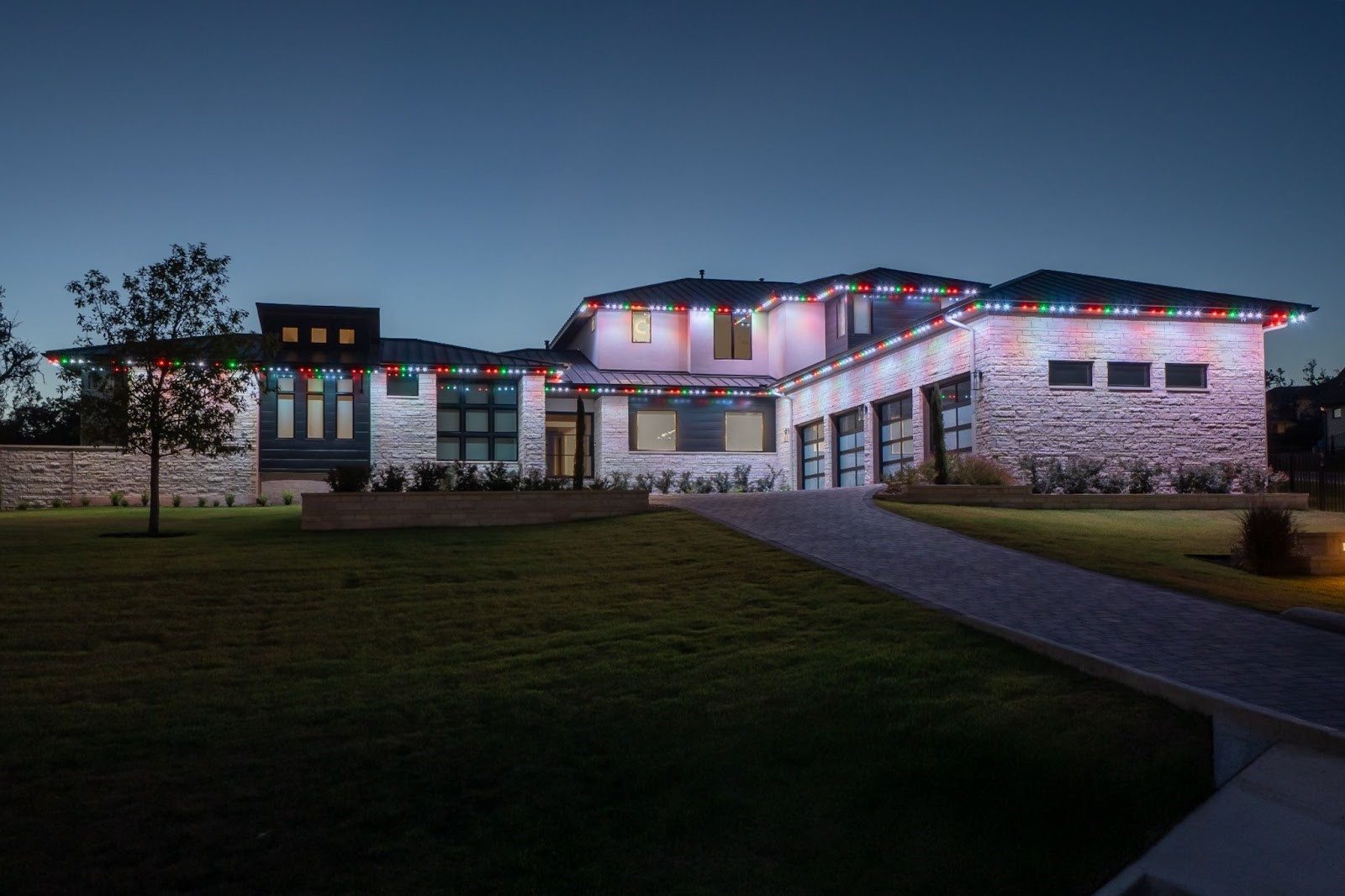 A luxurious home beautifully illuminated with green, red, and yellow Astoria Lighting Co. lights. The vibrant and elegant lighting highlights the intricate architectural details, creating a warm and festive ambiance