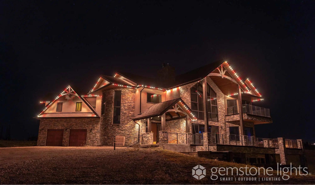 Rustic-style home illuminated with red and white smart outdoor lighting along the roofline, installed by Astoria Lighting Co.
