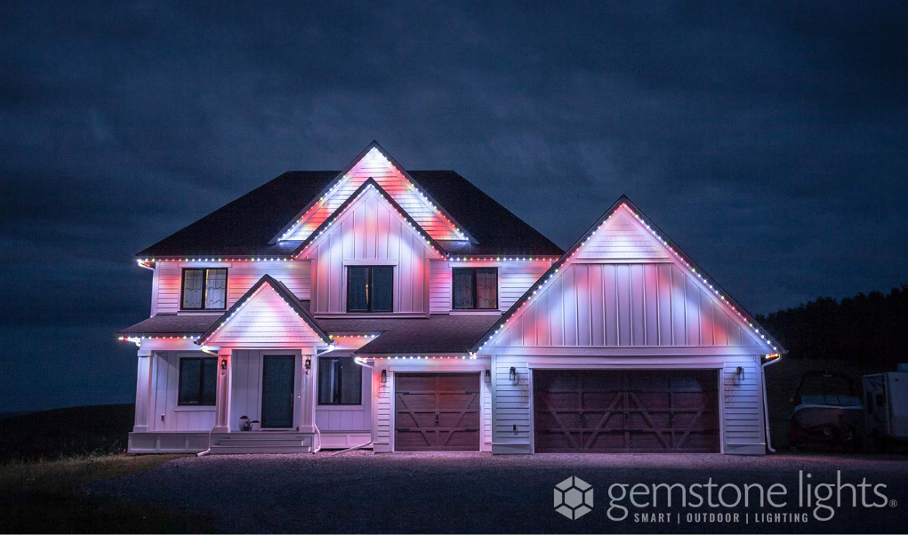 Two-story suburban home illuminated with customizable red, white, and blue smart outdoor lighting along the roofline, installed by Astoria Lighting Co.