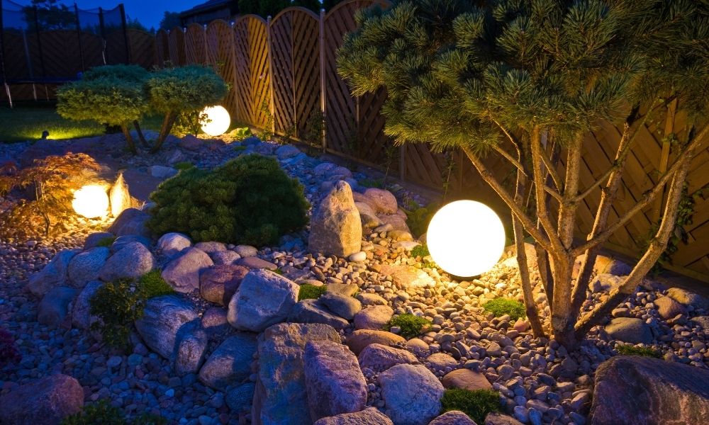 Landscape lighting illuminates Outdoor Living Spaces and a stone pathway and garden at dusk.
