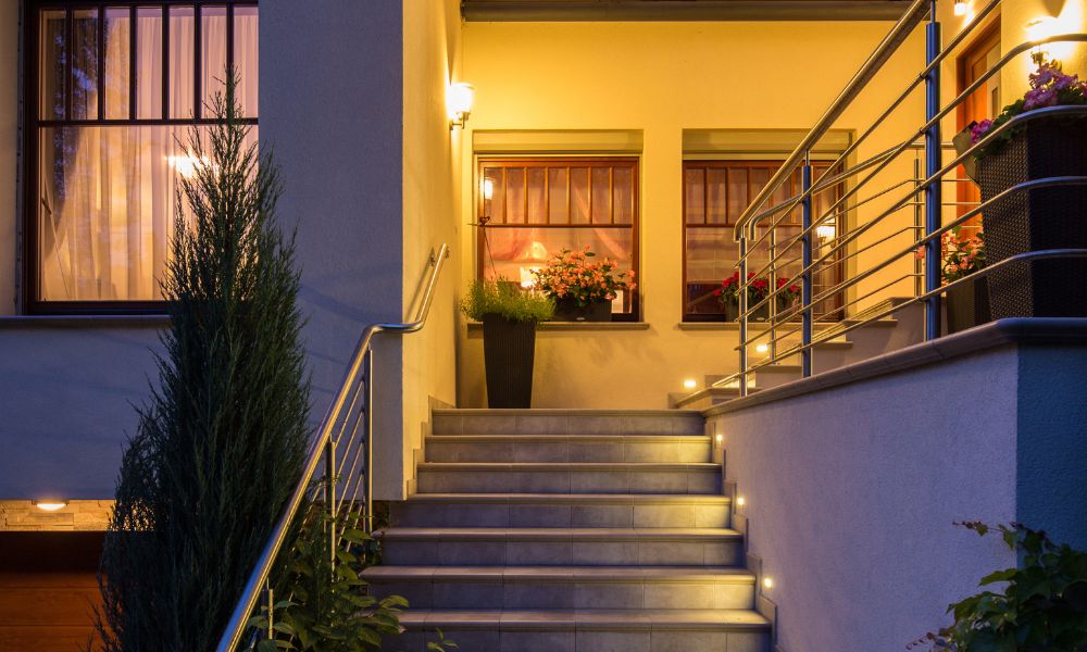 An elegant outdoor staircase leading to the entrance of a warmly lit house at night.