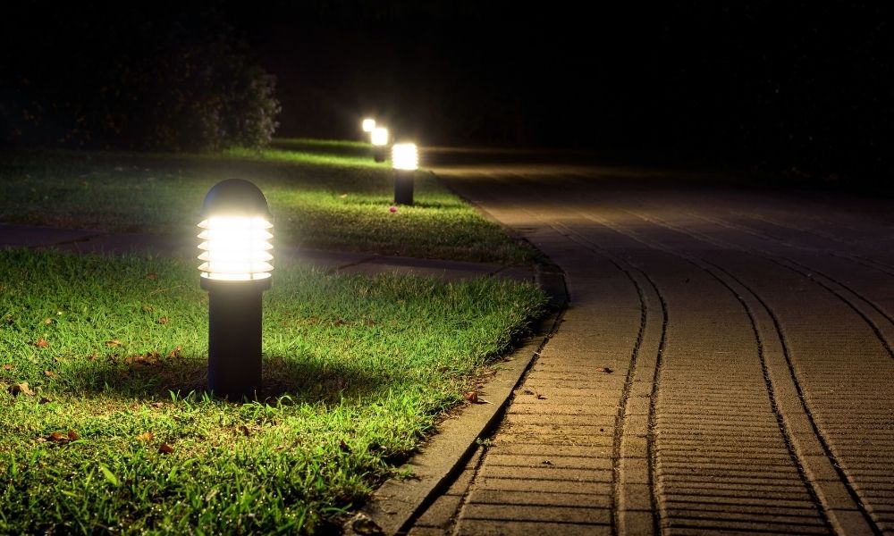 A landscaped backyard path is illuminated with warm lights on the floor.