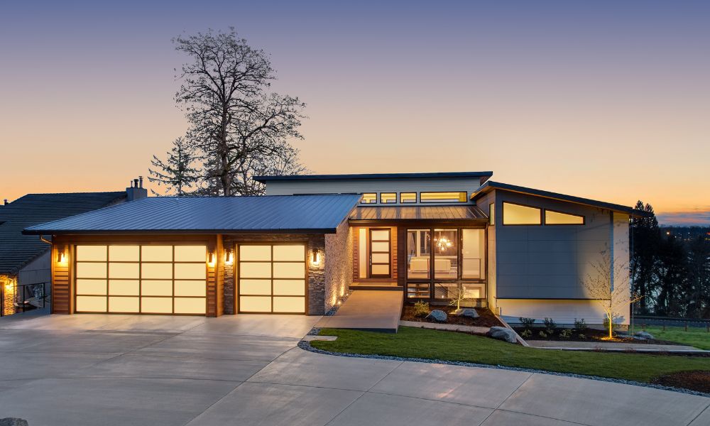 A modern single-story home illuminated at dusk. Warm outdoor lighting highlights the architectural lines