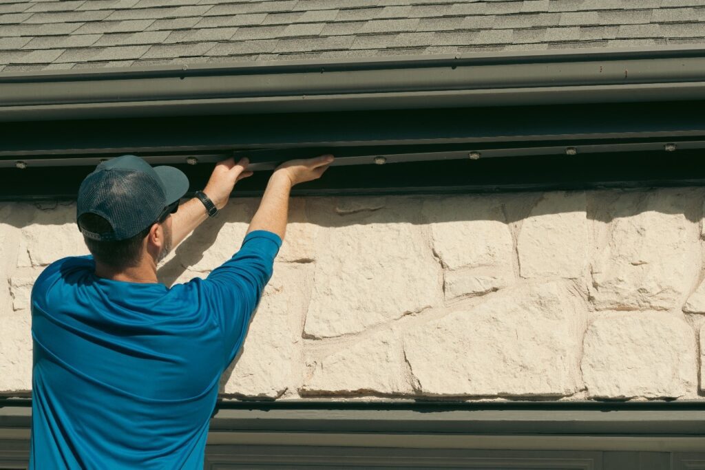 A male Astoria Lighting Co. employee installing permanent outdoor lights along a rooftop line. He is carefully securing the lights.