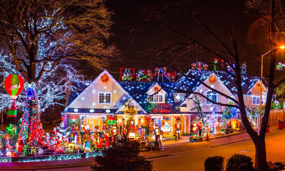 A house decorated with a display of Christmas lights and festive ornaments, featuring illuminated trees, Santa figures, and colorful holiday decorations