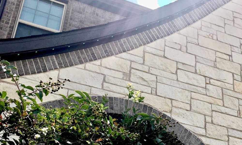 Close-up view of a modern home's exterior featuring a curved stone archway, black trim, and subtle green LED lights installed along the roofline