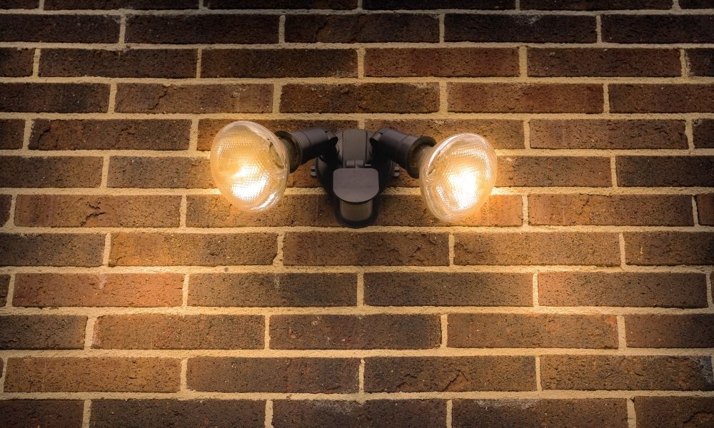 A motion-activated security light fixture mounted on a brick wall.
