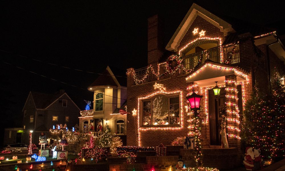 A house decorated with permanent Christmas lights and festive ornaments, featuring illuminated trees and bushes.