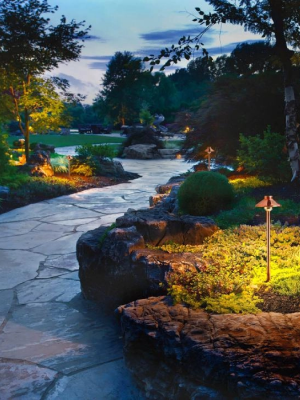 Landscape lighting illuminating a stone pathway and garden at dusk.