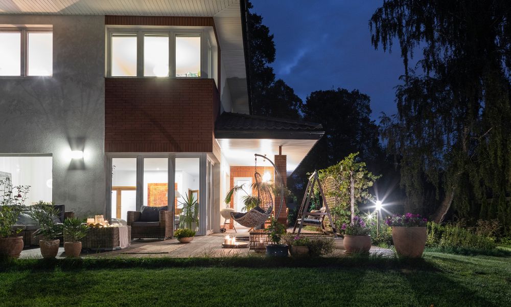 A modern two-story house with a cozy, well-lit backyard patio at night.