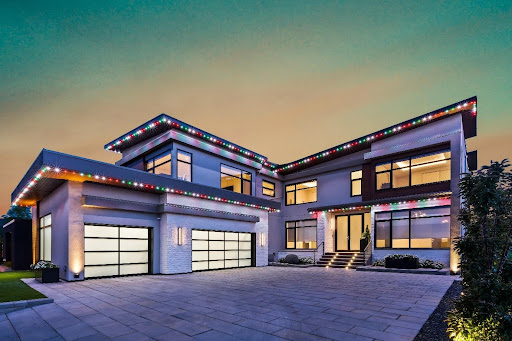A modern two-story home with sleek architecture, large glass windows, and a spacious driveway, illuminated by vibrant Astoria Lighting Co. smart outdoor lights. The customizable lighting enhances the clean lines of the home.