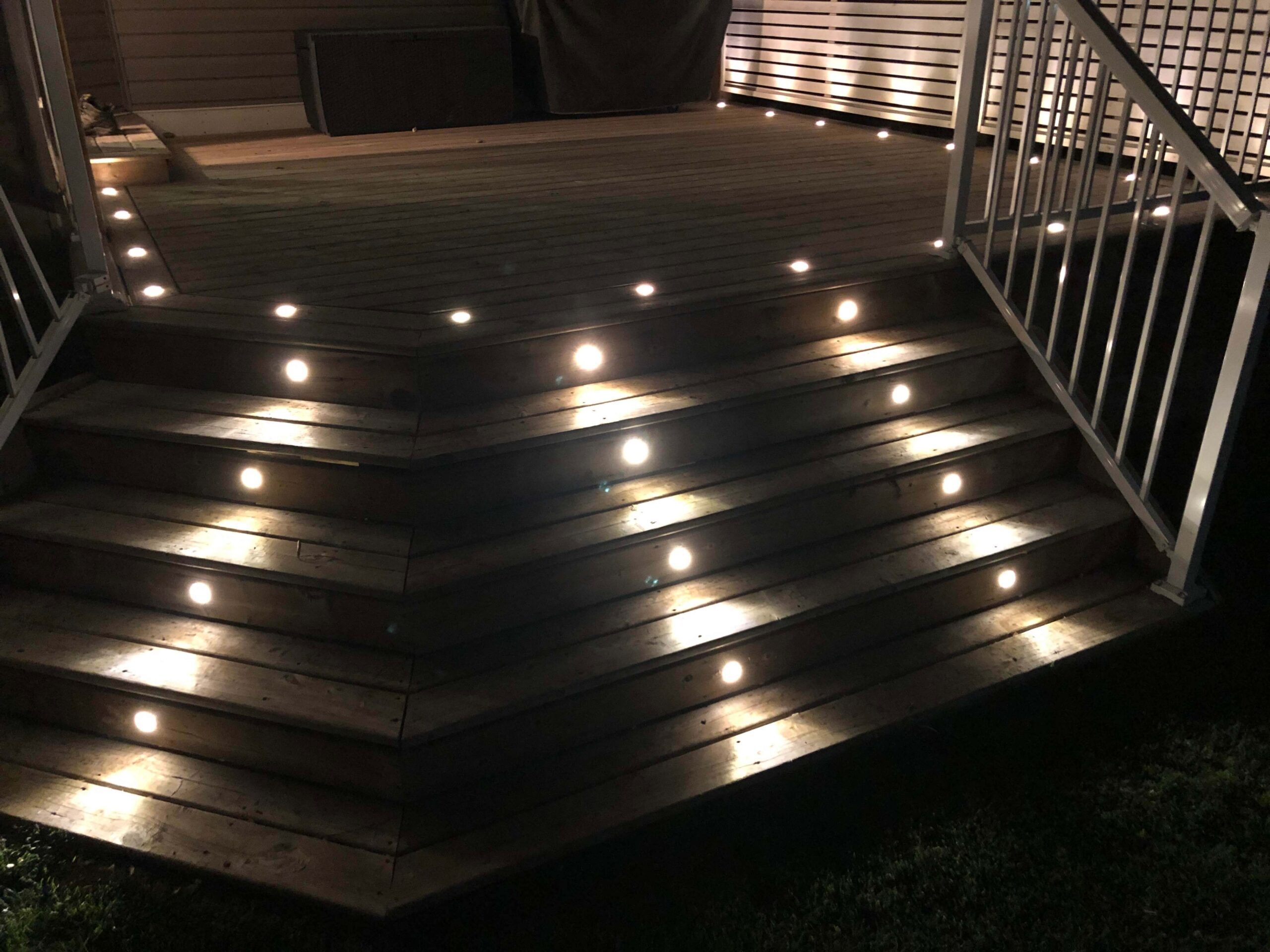 Residential backyard patio featuring Astoria’s closed-track permanent lighting system installed along the deck and steps, showcasing warm ambient lighting that enhances outdoor safety and style.