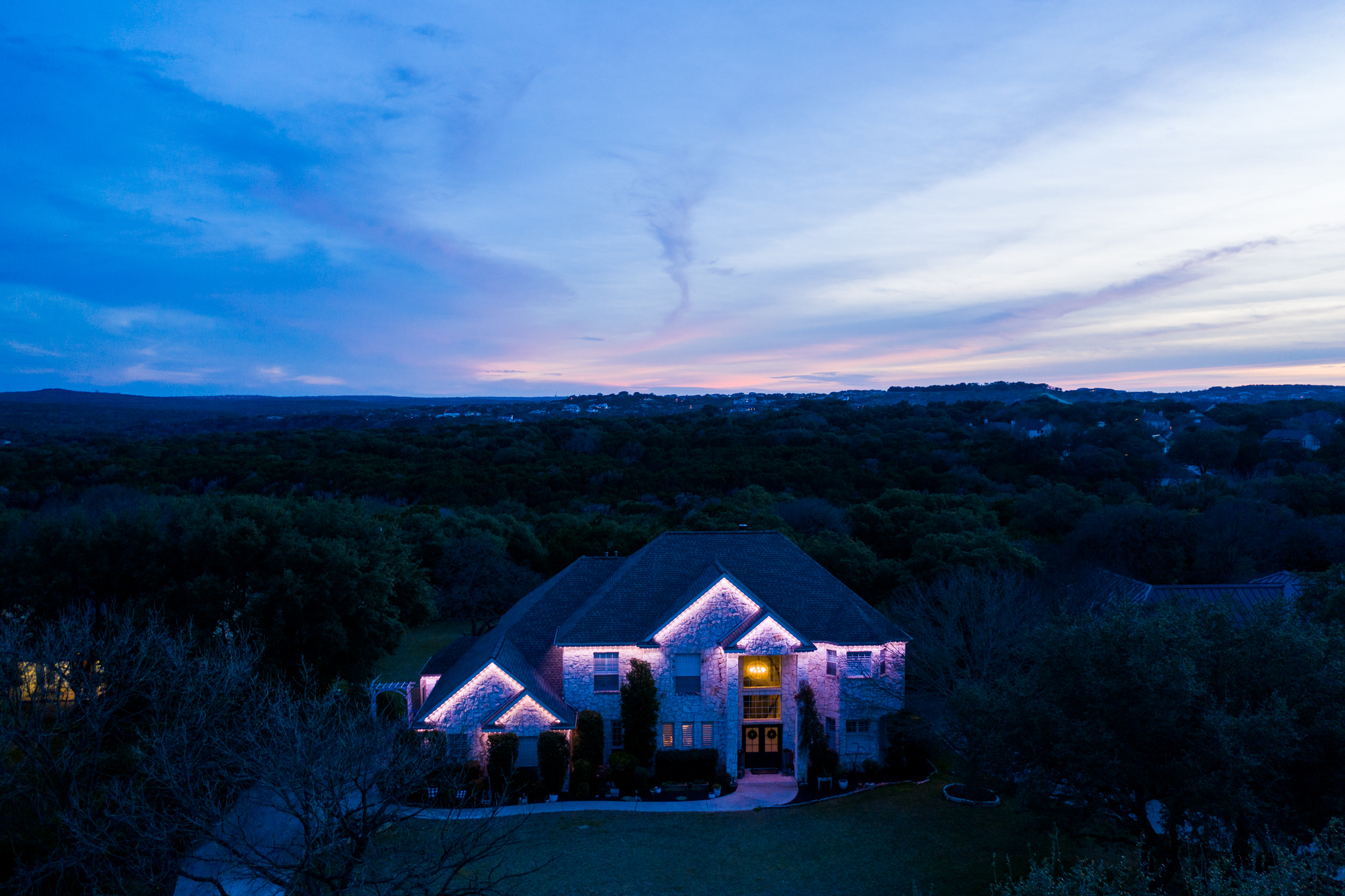 Aerial view of a luxury natural stone home featuring Astoria’s soffit-fitted permanent Christmas lighting system, accentuating the roofline with elegant illumination and architectural detail.