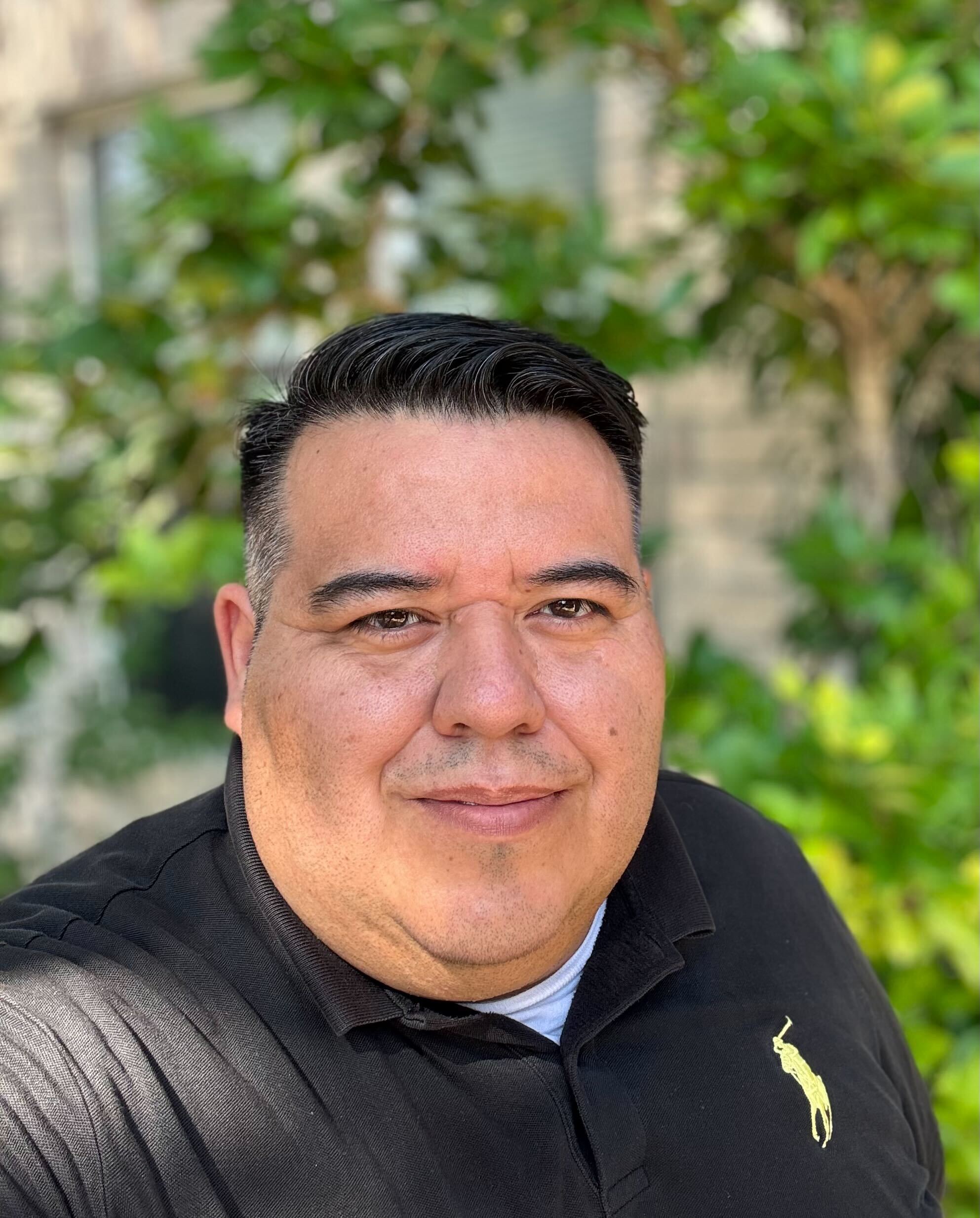 Professional headshot of the San Antonio, TX branch general manager at Astoria Lighting Co., photographed outdoors with a tree in the background.