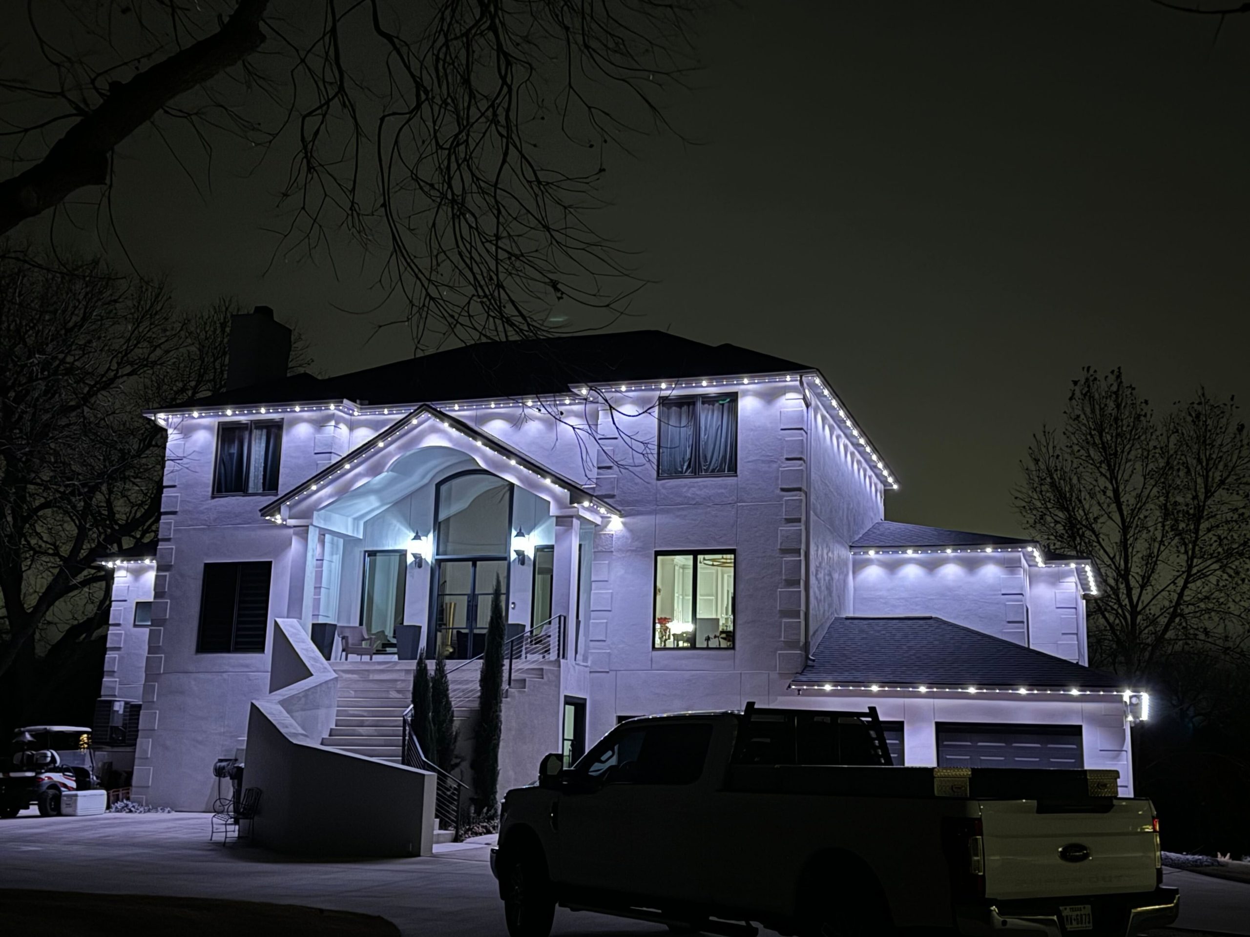 Two-story white exterior home featuring Astoria’s permanent holiday lighting system installed along the soffit, displaying cool white lights that highlight the roofline and enhance security and safety.