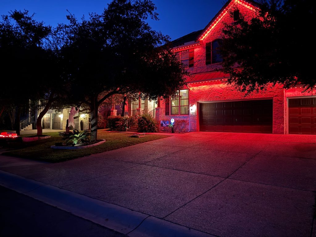 Residential stone home featuring Astoria’s permanent holiday lights installed along the soffit line displaying bold red light.