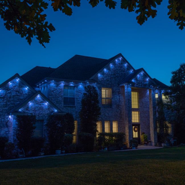 Luxury organic stone house featuring Astoria permanent lighting system along soffit line displaying cool white light pattern.