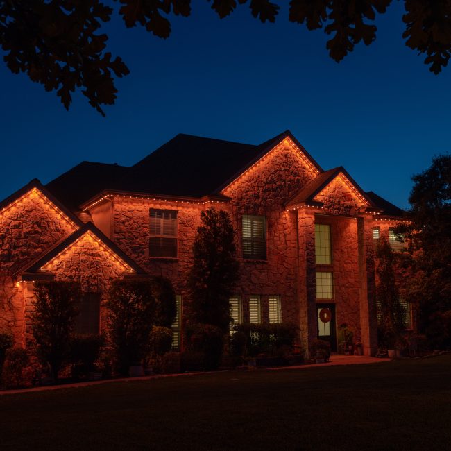 Luxury organic stone house featuring Astoria permanent lighting system along soffit line displaying Halloween theme solid orange light.