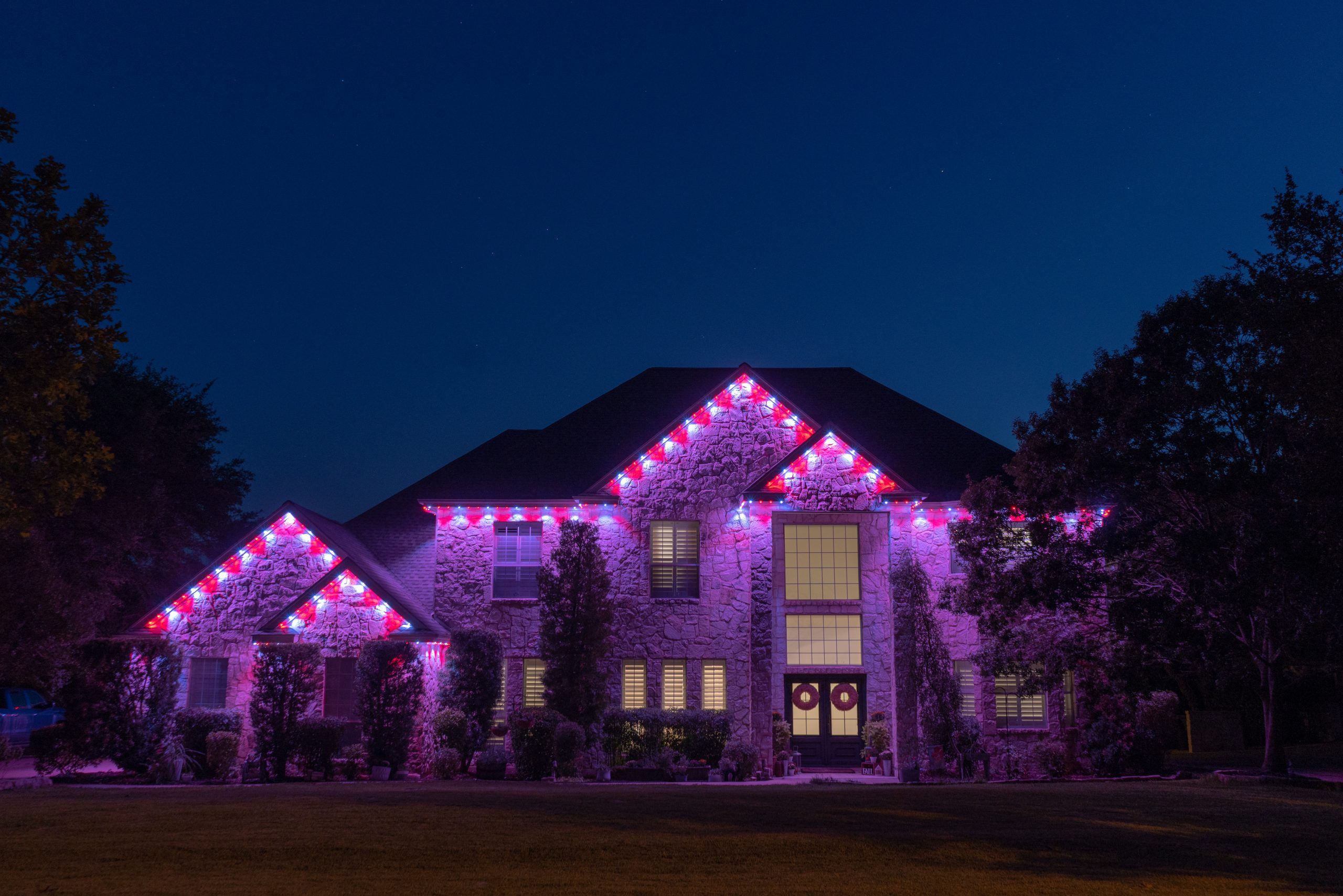 Luxury organic stone house featuring Astoria permanent lighting system along soffit line displaying valentine theme pink and white color pattern.