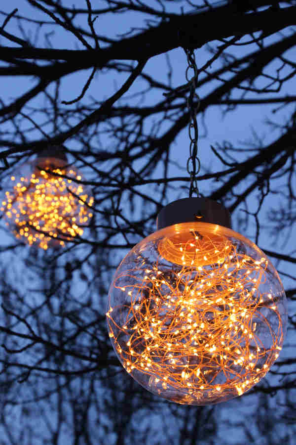 Astoria signature Firefly globe fixtures hanging from tree branches at sundown.