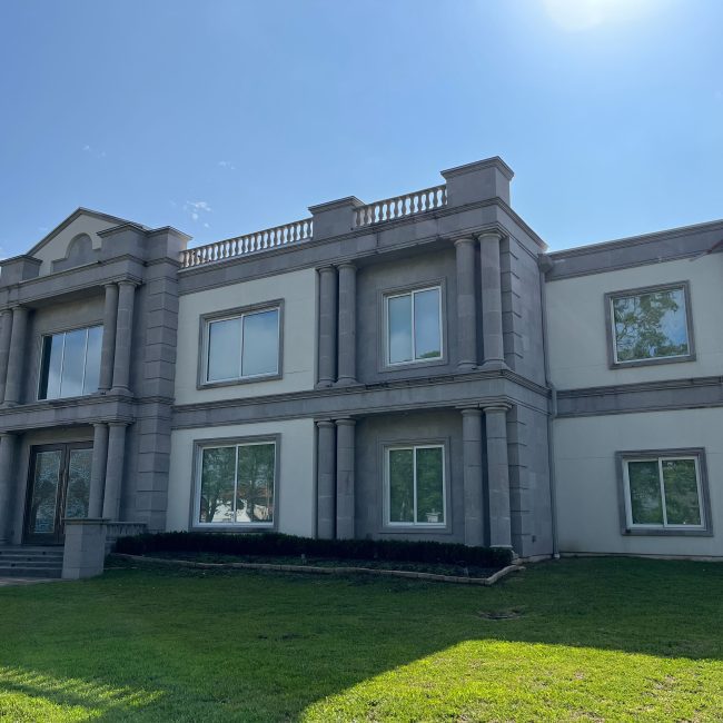 Astoria installer on a ladder installing Astoria’s permanent lighting system along a luxury home’s soffit line during daylight.