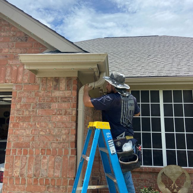 Astoria installer installing Astoria’s closed-track permanent lighting system along the soffit line of a brick home.