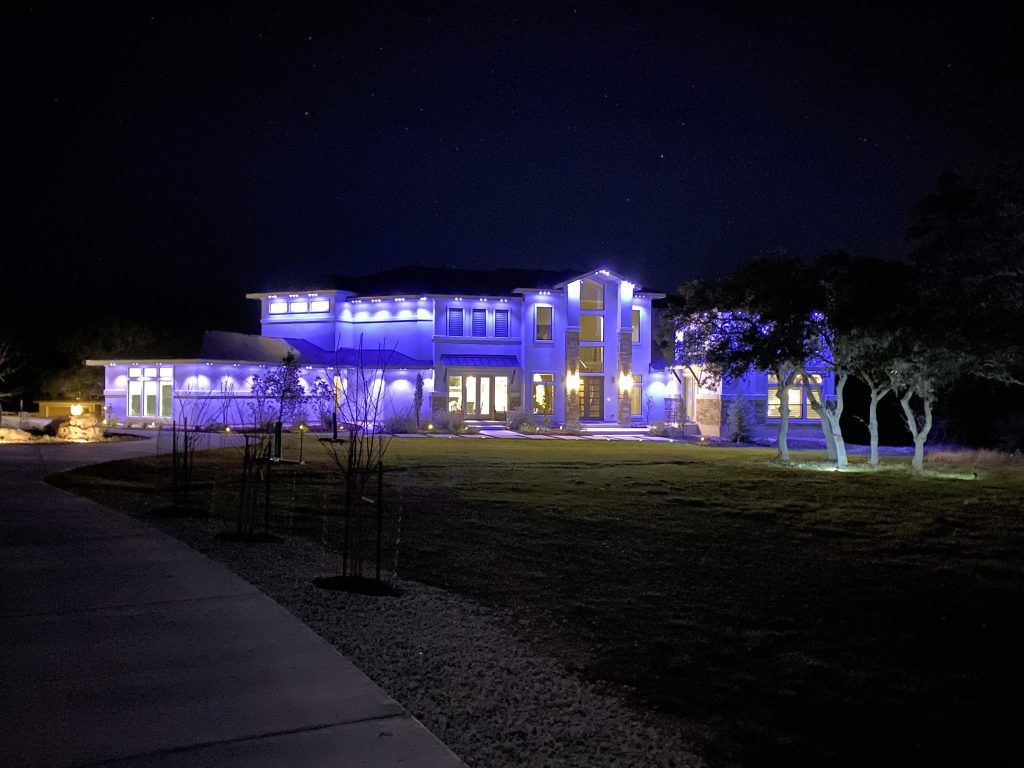 Luxury two story home featuring Astoria permanent holiday lighting system displaying cool blue lights under night sky.